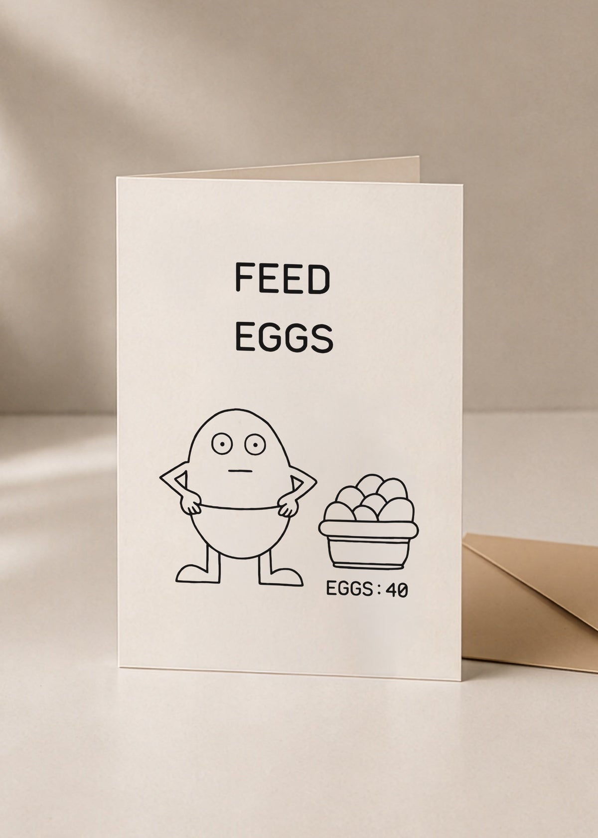 Feed Eggs illustrated greeting card standing beside a kraft envelope on a cream surface.