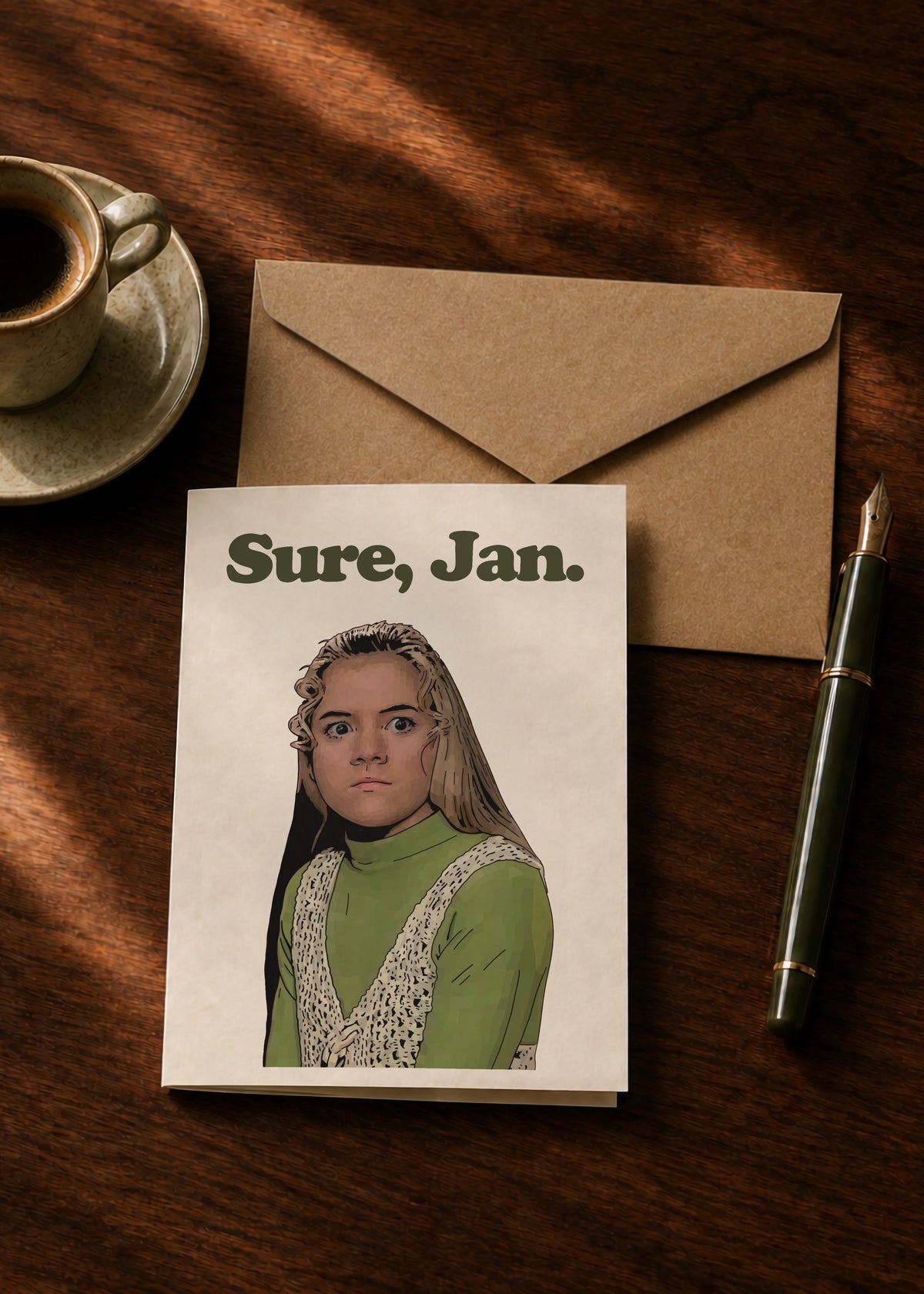 Sure, Jan. greeting card and kraft envelope on a dark wooden table beside a coffee cup and fountain pen.